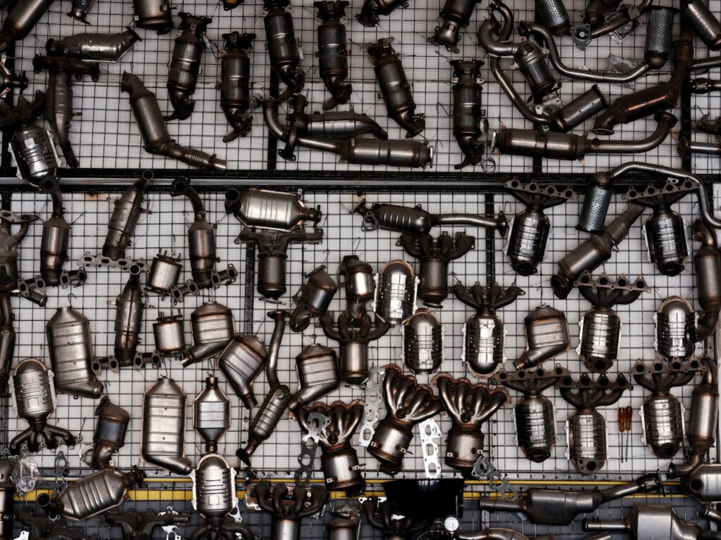 An array of automotive exhaust parts displayed on a grid wall in an industrial garage setting.
