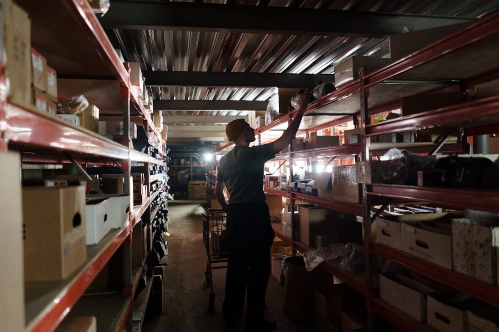 pexels-photo-7019222 A worker arranging inventory on shelves in a dimly lit warehouse, utilizing efficient storage practices.